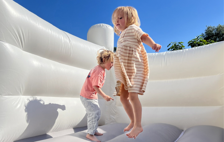 niños saltando en castillo hinchable blanco frente a cielo azul